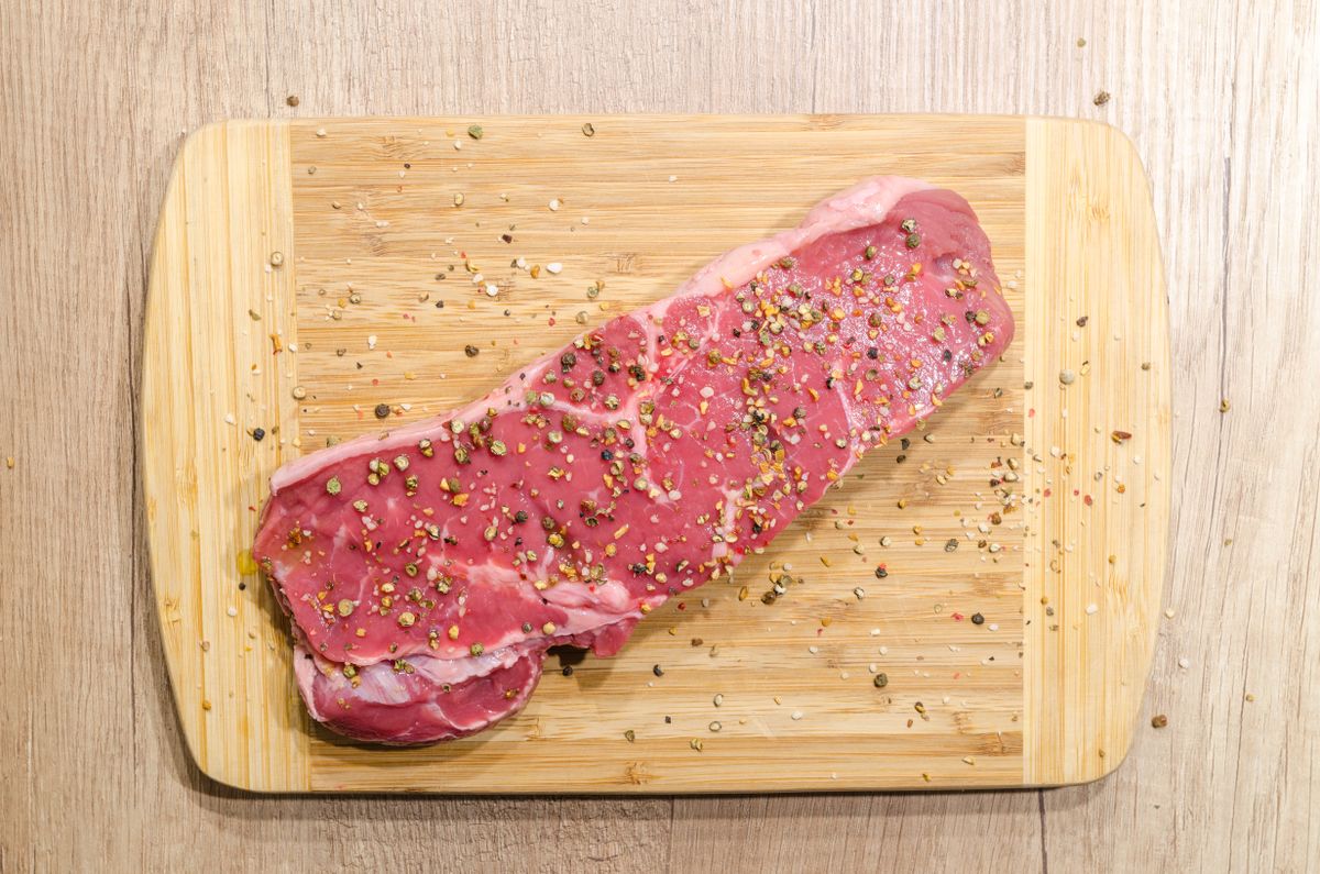 Corte de carne cruda con especias sobre tabla de madera